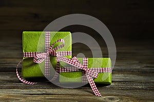 Two green gifts with red white checkered ribbon on wooden background.