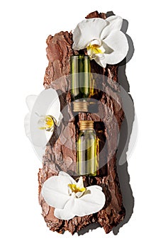Two green glass cosmetic bottles on textured tree bark podium with white orchid flowers in rays of sunlight with hard