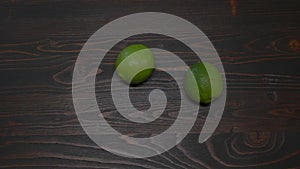 Two green limes roll on a wooden table