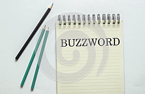 Two green one black pencil with text BUZZWORD in the notebook on the white background