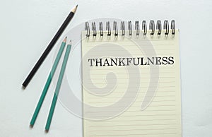 Two green one black pencil with text Thankfulness in the notebook on the white background