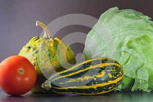 Two green and orange pumpkin on stone desk with tomato and lettuce