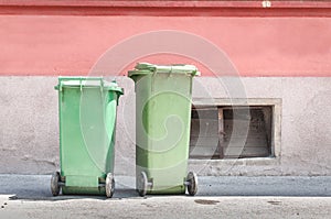 Two green plastic garbage cans on the street with junk and litter waiting for dumpster truck to collect the trash