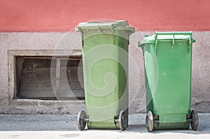 Two green plastic garbage cans on the street with junk and litter waiting for dumpster truck to collect the trash