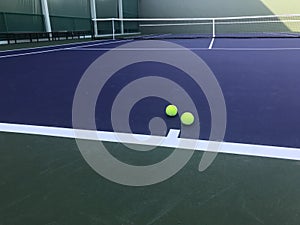 Two green tennis balls put on blue tennis court with net on background