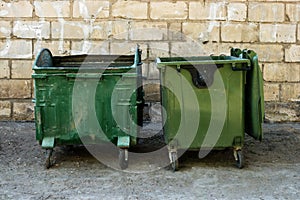 Two Green Trash Dumpsters In Front Of White Brick Wall Front View With Room For Text. Garbage Cans in Front of Warehouse Wall.