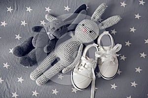 Two grey knitted toy rabbit and children`s white shoes