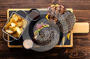 Two grilled burgers with beef cutlet, sauce and French fries on a wooden board, top view. Fast food set