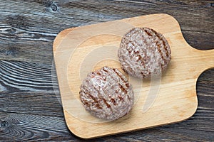 Two grilled hamburger patties on wooden background