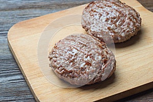 Two grilled hamburger patty on cutting board