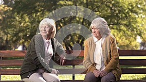 Two grumpy old ladies judging passerby people, sitting on bench in park, pension photo