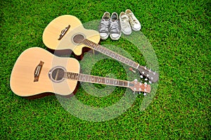 Two guitars and two pairs of shoes on bright green grass texture