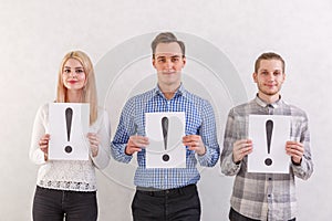 Two guys and a girl with light smiles are standing next to keep the sheets with exclamation marks on a gray background