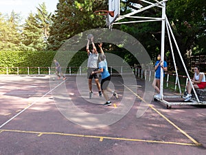 Two guys playing basketball and one guy playing soccer on an outdoor basketball court