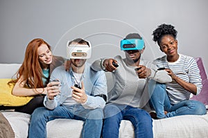Two guys playing video games using VR glasses and girlfriends support them.