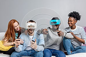 Two guys playing video games using VR glasses and girlfriends support them.