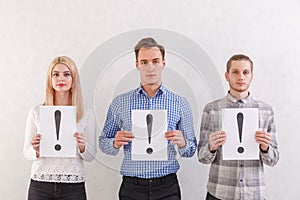 Two guys and a girl stand next to keep the sheets with exclamation marks on a gray background