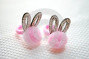 Two hair scrunchies with black ears in rhinestones and a soft pink pompom on white table