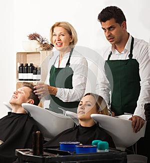 Two hairstylists working with hair of clients in washing tray