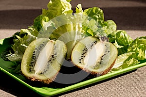 Two half juicy ripe kiwi fruit, fresh lettuce on plastic plate. Green background. Salad leaves. Organic healthy food. Detox diet