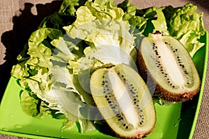 Two half juicy ripe kiwi fruit, fresh lettuce on plate. Saturated green background. Salad leaf. Organic healthy food. Detox diet