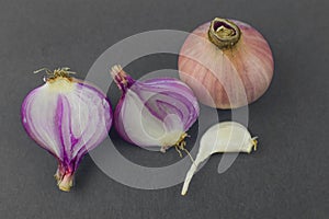 Two half peeled pink colored onion beside a unpeeled onion and a piece of garlic seed