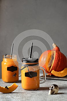 Two Halloween Cocktails with pumpkin juice garnish skull and spiders for festive party on gray