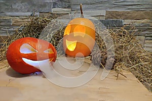 Two halloween jack o lanterns yellow and red with smoke on foreground on a hay and brick wall background. with cones on wooden