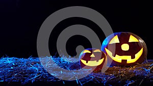 Two Halloween pumpkins are burning bright flames inside are standing on hay. Black background