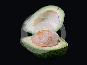 Two halves of avocado with bone, on a black background. Green, ripe avocado vegetable in a cut. Halves Persea