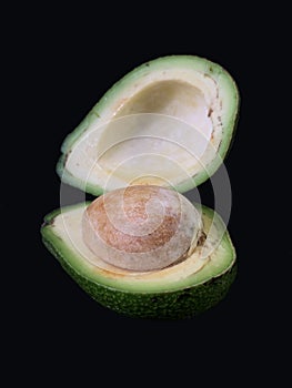 Two halves of avocado with bone, on a black background. Green, ripe avocado vegetable in a cut. Halves Persea
