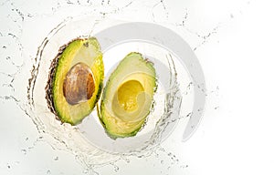 Two halves of avocado splashing into water, isolated on white background. Copy space