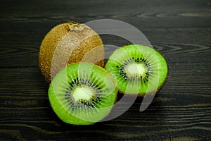 Two halves bright juicy ripe beautiful kiwi and a whole kiwi on a coarse dark wooden background from boards