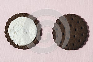 Two halves of chocolate-cream cookies on a pink background