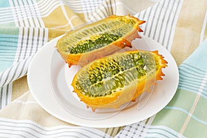 Two halves of fresh orange kiwano cucumis metuliferus, horned melon on a white plate over a table. Fruits, vegetables,