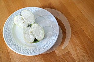 Two halves of a green apple are sprinkled with sugar on a plate and on a wooden table, minimalism