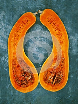 Two halves of a pear-shaped pumpkin of orange color, are located on a background of turquoise color vertically