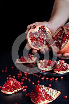 Two halves of pomegranate in male hands. On the table is a pomegranate.