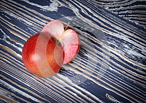 Two halves of a red apple are on a wooden surface