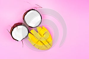 Two halves of a ripe coconut with a ripe mango half on a pink background.