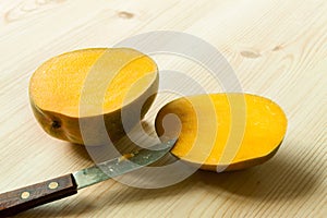 Two halves sliced exotic fruit mango with knife on the wooden table board.