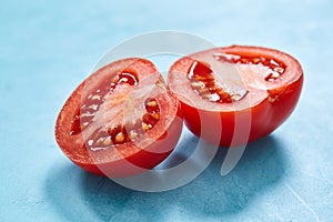 Two halves of tomato placed on blue background, top view, close-up, shallow depth of field.