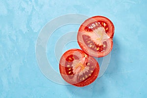 Two halves of tomato placed on blue background, top view, close-up, shallow depth of field.