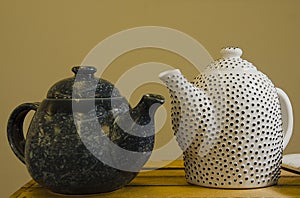 Two handmade teapots on a wooden shelf in the market. White ceramic teapot in the black dot. Dark teapot.