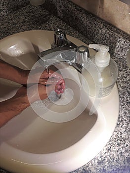 Two hands are cleaned in a cream colored sink washing with soap and water creates bubbles photo