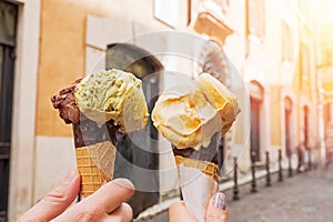 Two hands close-up holding cones with italian ice-cream gelato on the background of Rome streeet