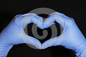 Two hands covered in blue surgical gloves, forming a heart, on a black background