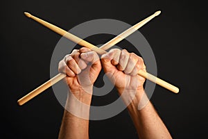 Two hands with crossed drumsticks over black