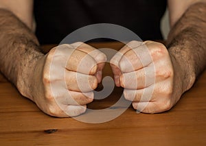 Two hands fists on wooden table clench hairy man fists symbol anger closeup