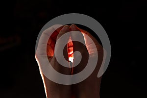 Two hands folded squeeze the light inside, reddish light inside the hands, black background.